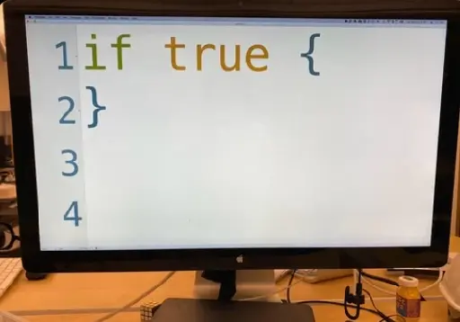Picture of a computer monitor showing a text editor with the code "if true {}". The font size is so big the code takes most of the width of the monitor.